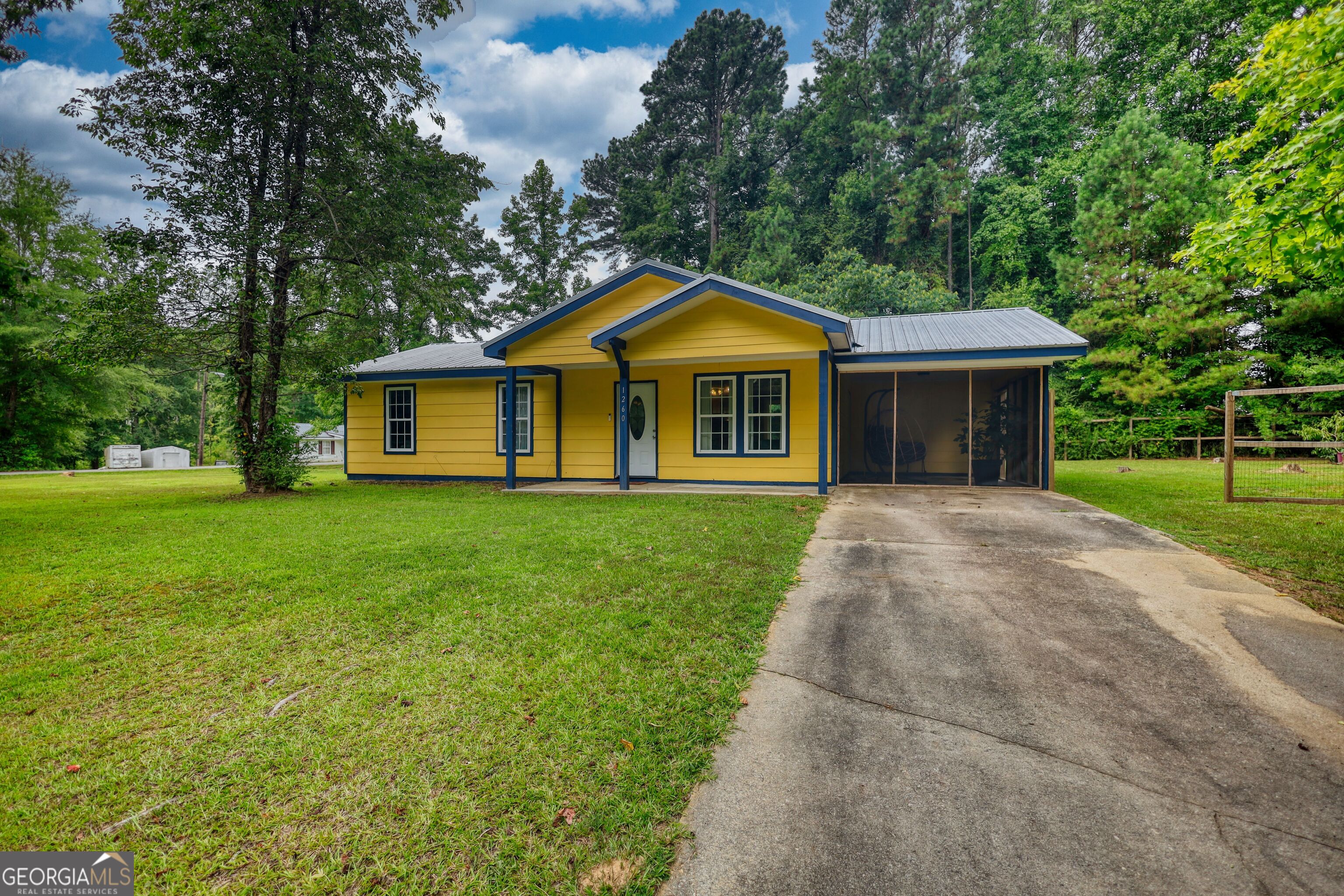 Yellow single-story house with blue trim, a metal roof, screened porch, and wide driveway.