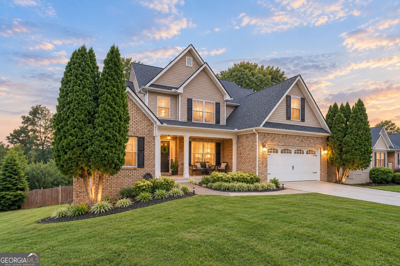 Two-story brick-and-siding home with a two-car garage and landscaped lawn at sunset.