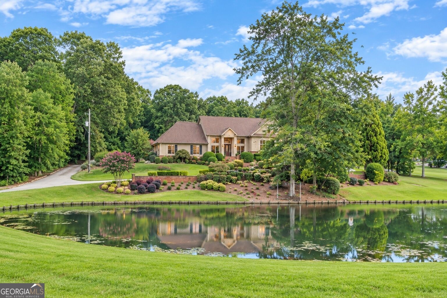 Single-story house with landscaped grounds and mature trees beside a pond.