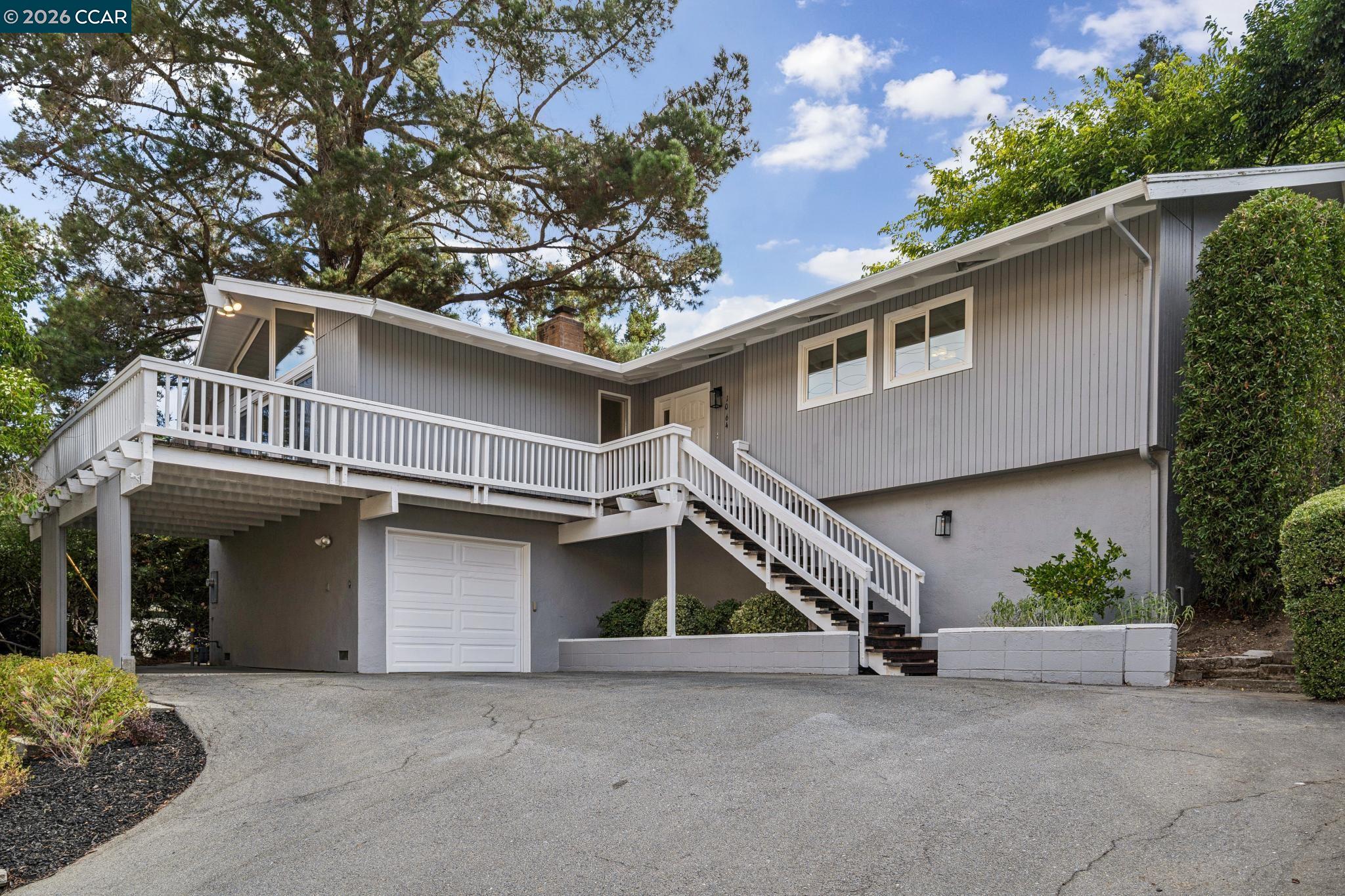 Gray split-level home's front exterior with an elevated white-railed deck, staircase, and attached garage.