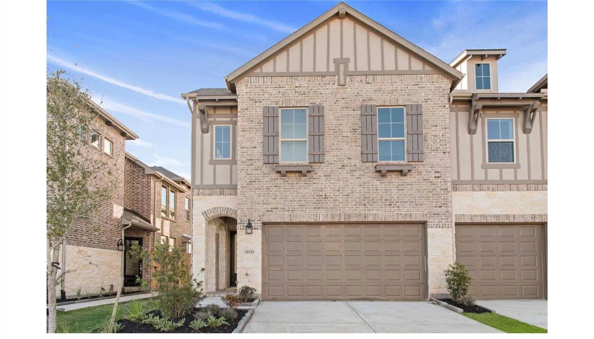 Two-story brick home with shuttered windows, an arched entry, and a two-car garage.