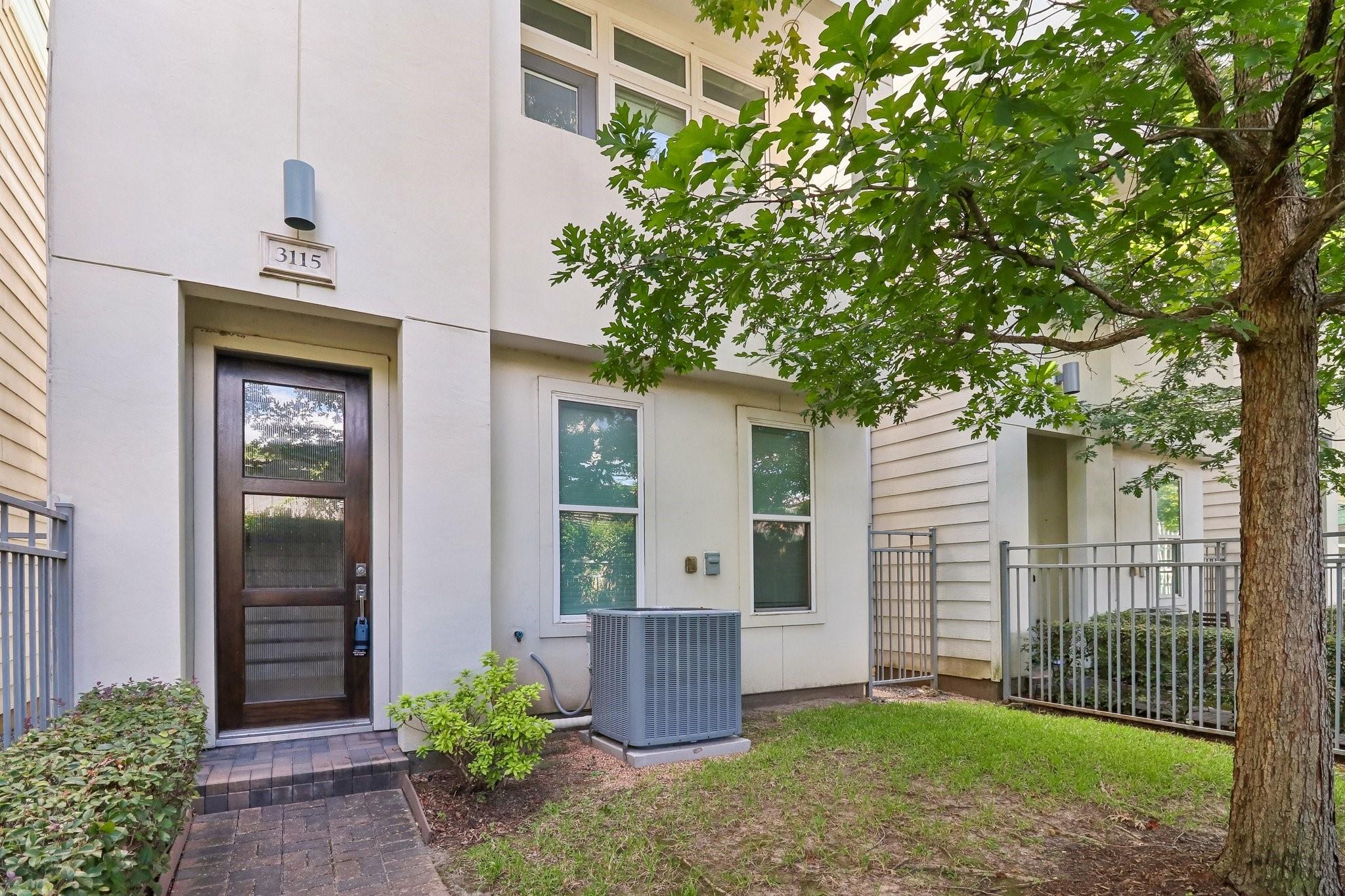 Townhouse entrance marked 3115, with a dark glass-paneled door beneath a leafy tree.