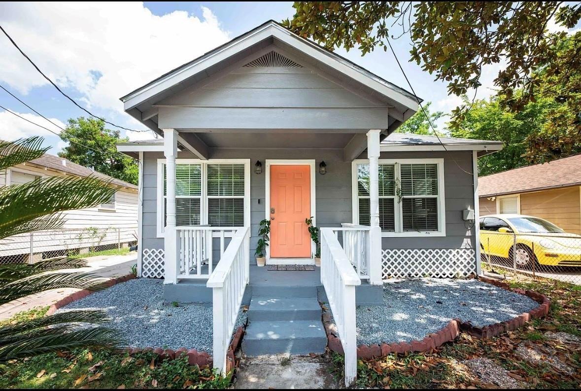 Gray house with a gabled porch, white railings, and a bright orange front door.