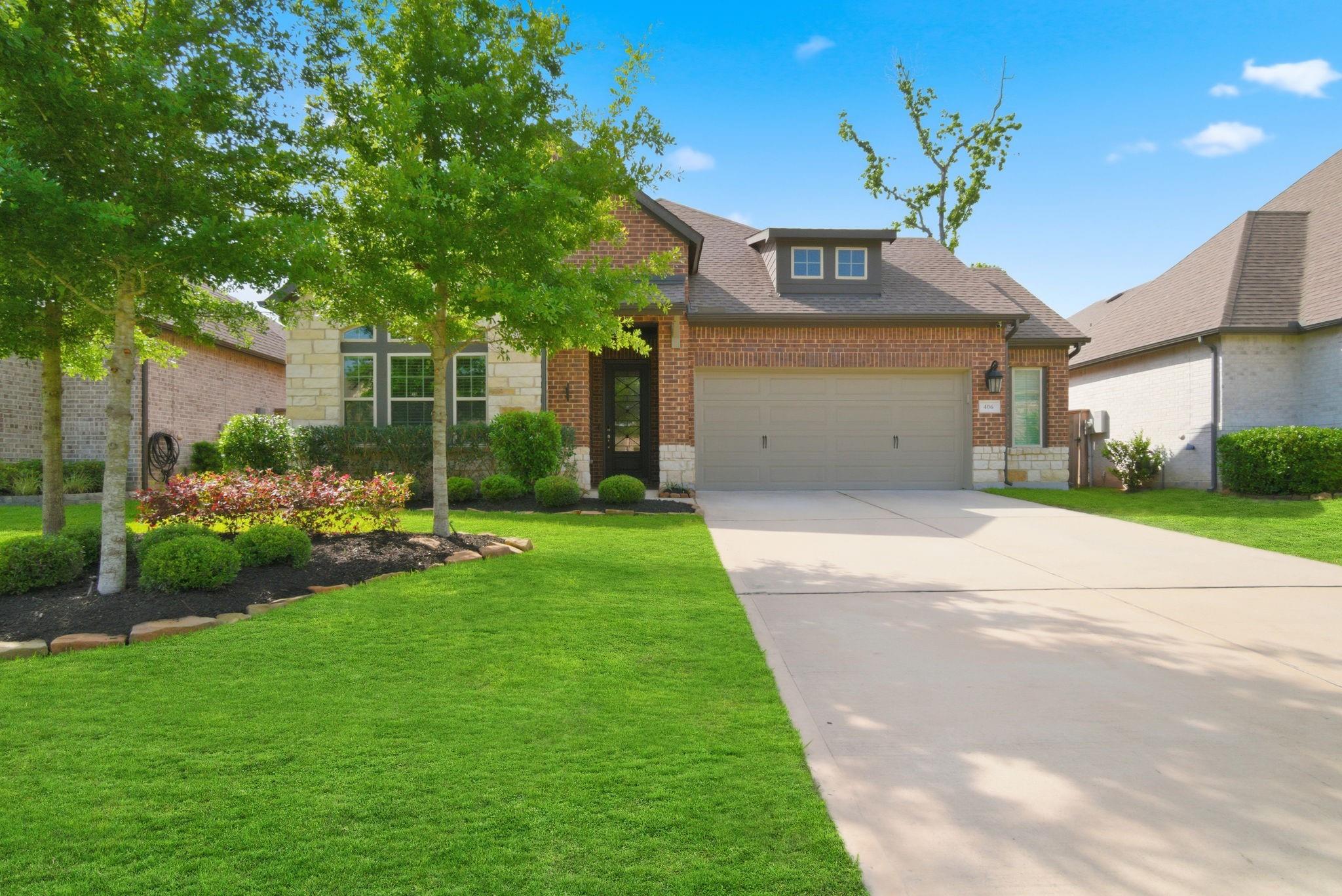 Brick-and-stone two-story home with a double garage, landscaped lawn, and mature trees.