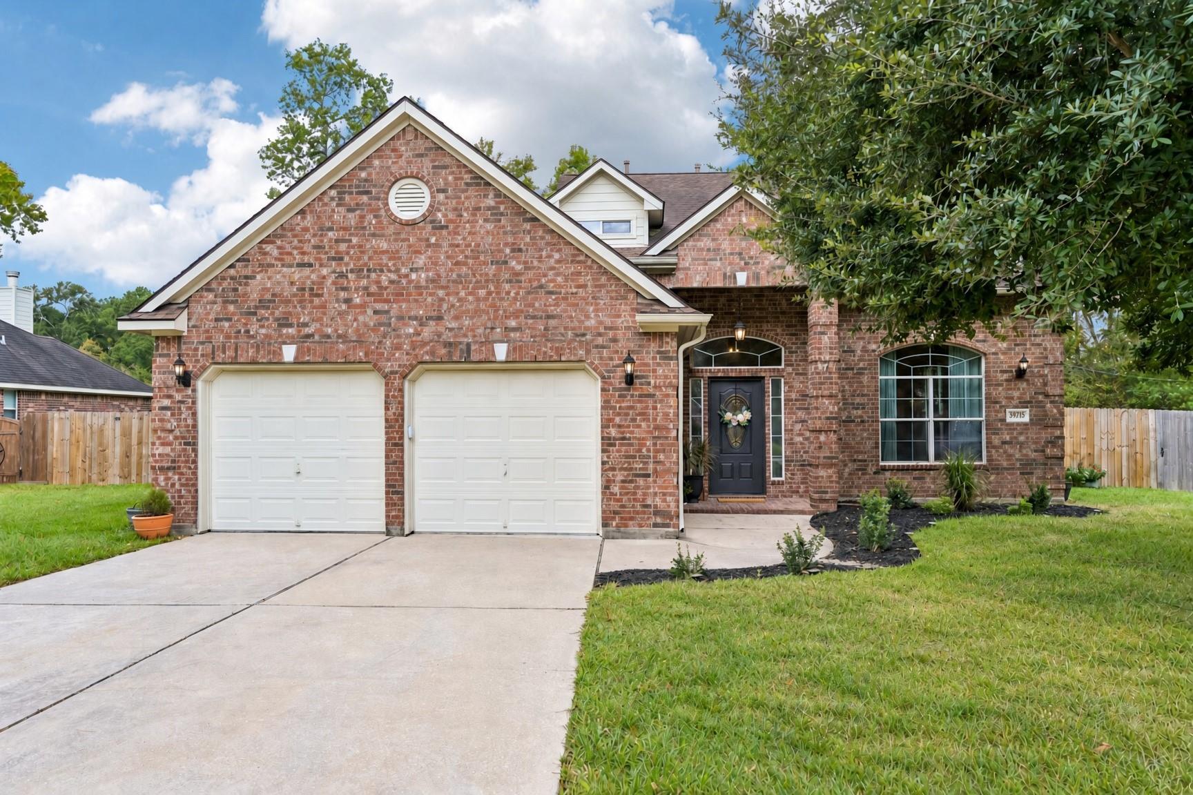 Red-brick home with two white garage doors, a covered entry, and a wide concrete driveway.