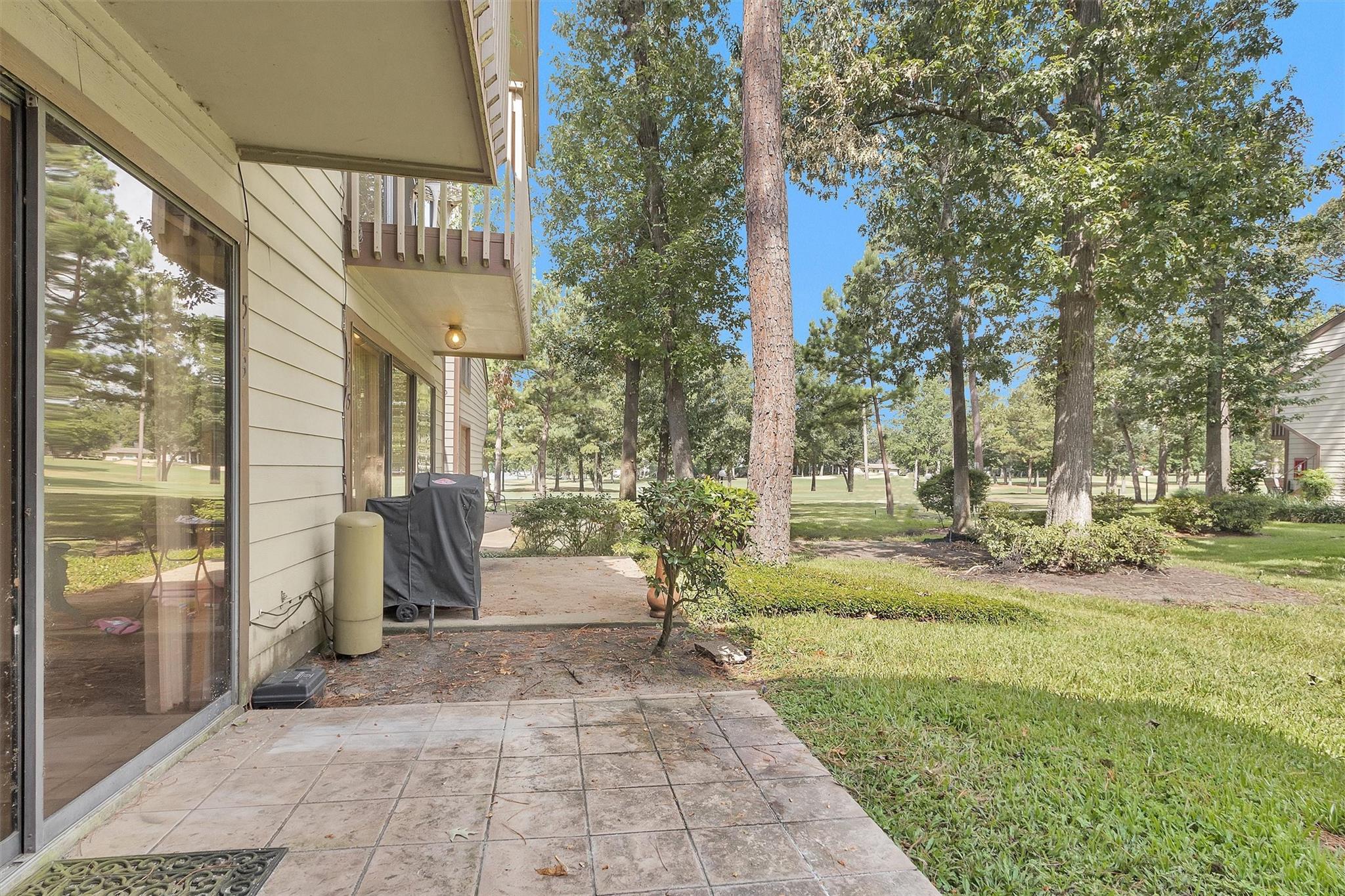 Home patio overlooking a tree-shaded lawn, with sliding doors and a covered grill.