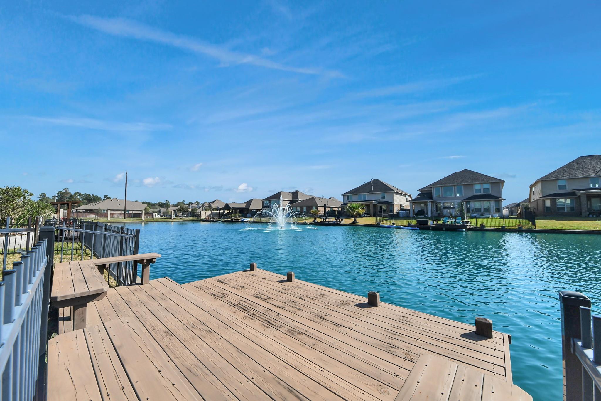 Waterfront dock overlooking a lake with a fountain and homes along the opposite shore.