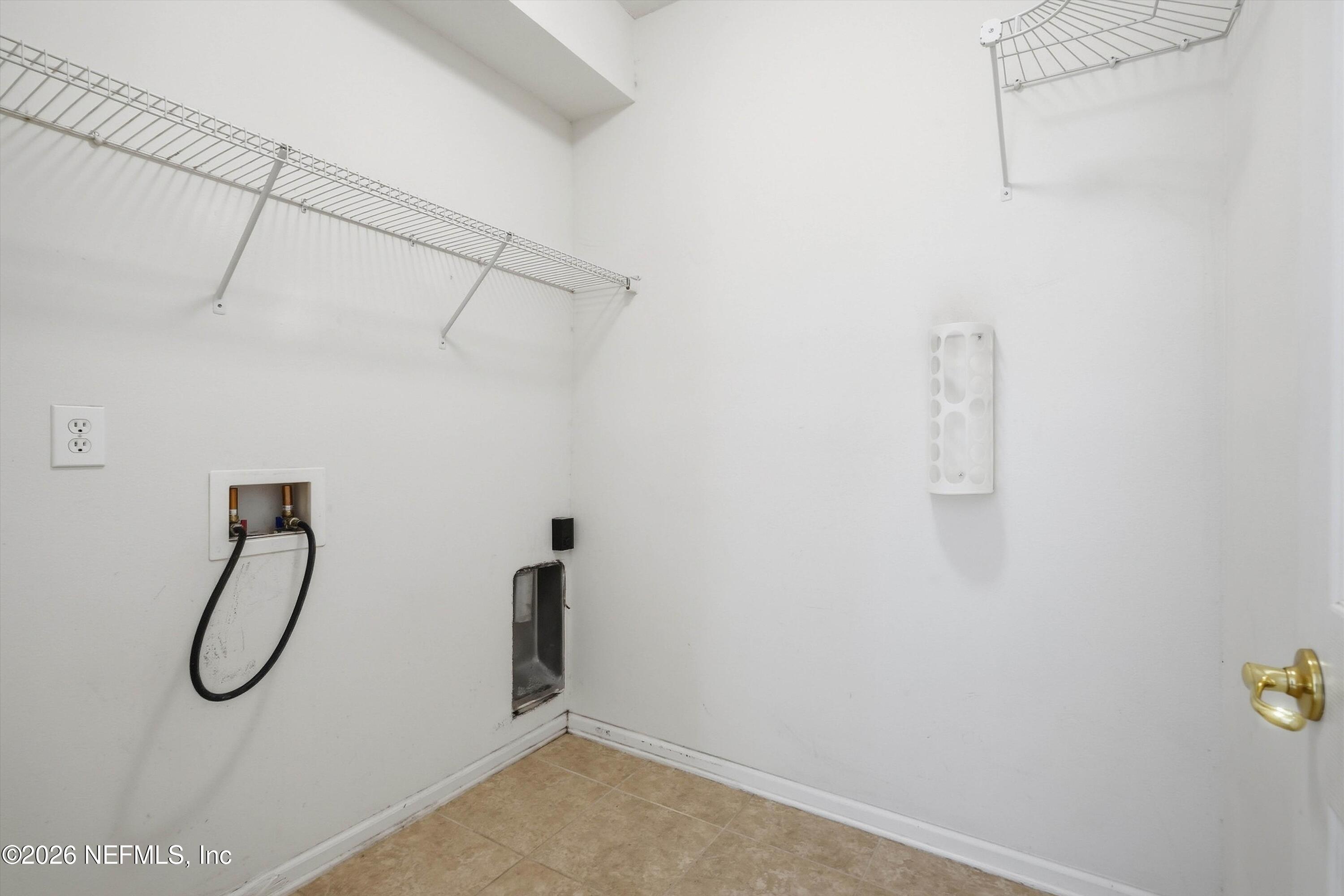 Vacant laundry room with wire shelves, washer hookups, and tan tile flooring.