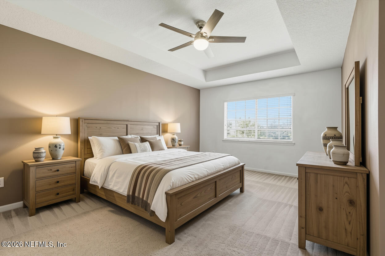 Staged bedroom with a wooden bed, white bedding, tray ceiling, and large window with blinds.