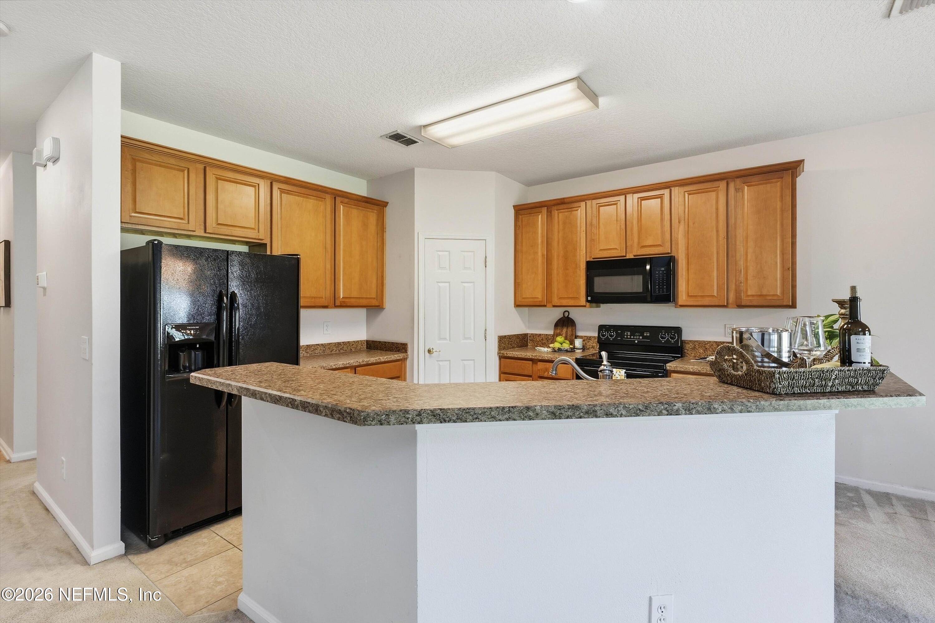 Kitchen with honey-toned cabinets, a broad peninsula, and black appliances.