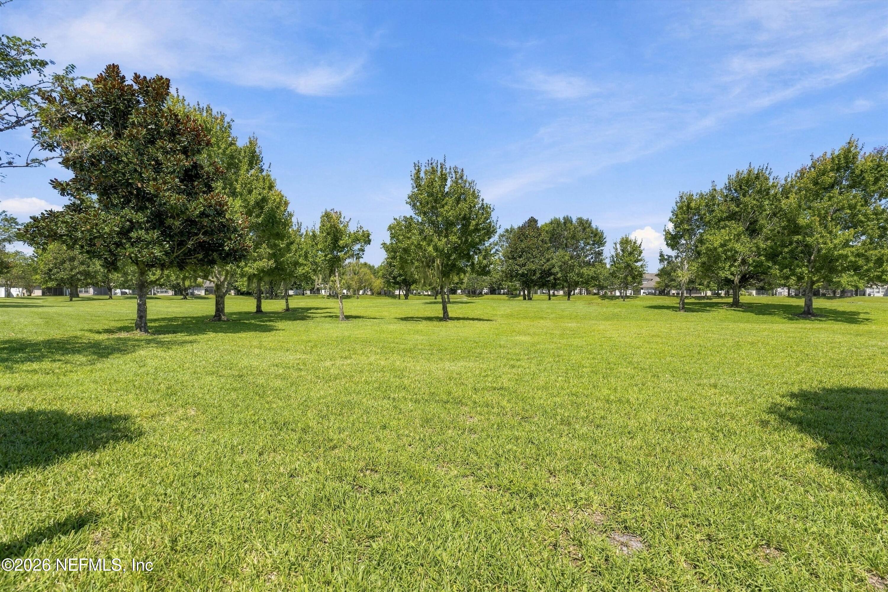 Open grassy area with scattered trees and distant homes.