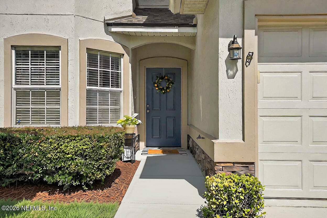 Home entrance with a dark blue front door, covered entry, trimmed hedges, and attached garage.