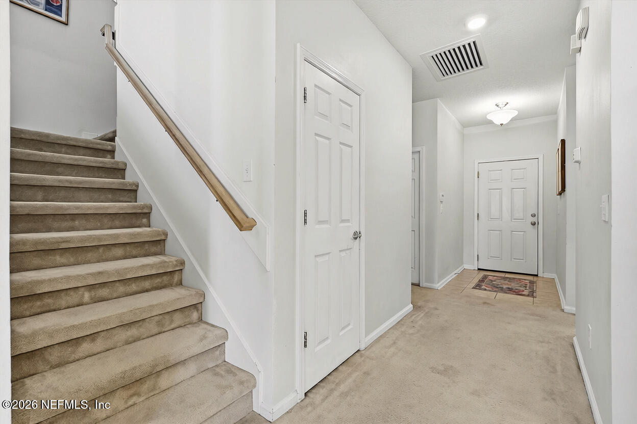 Entry hallway with a carpeted staircase, wood handrail, and white front door.