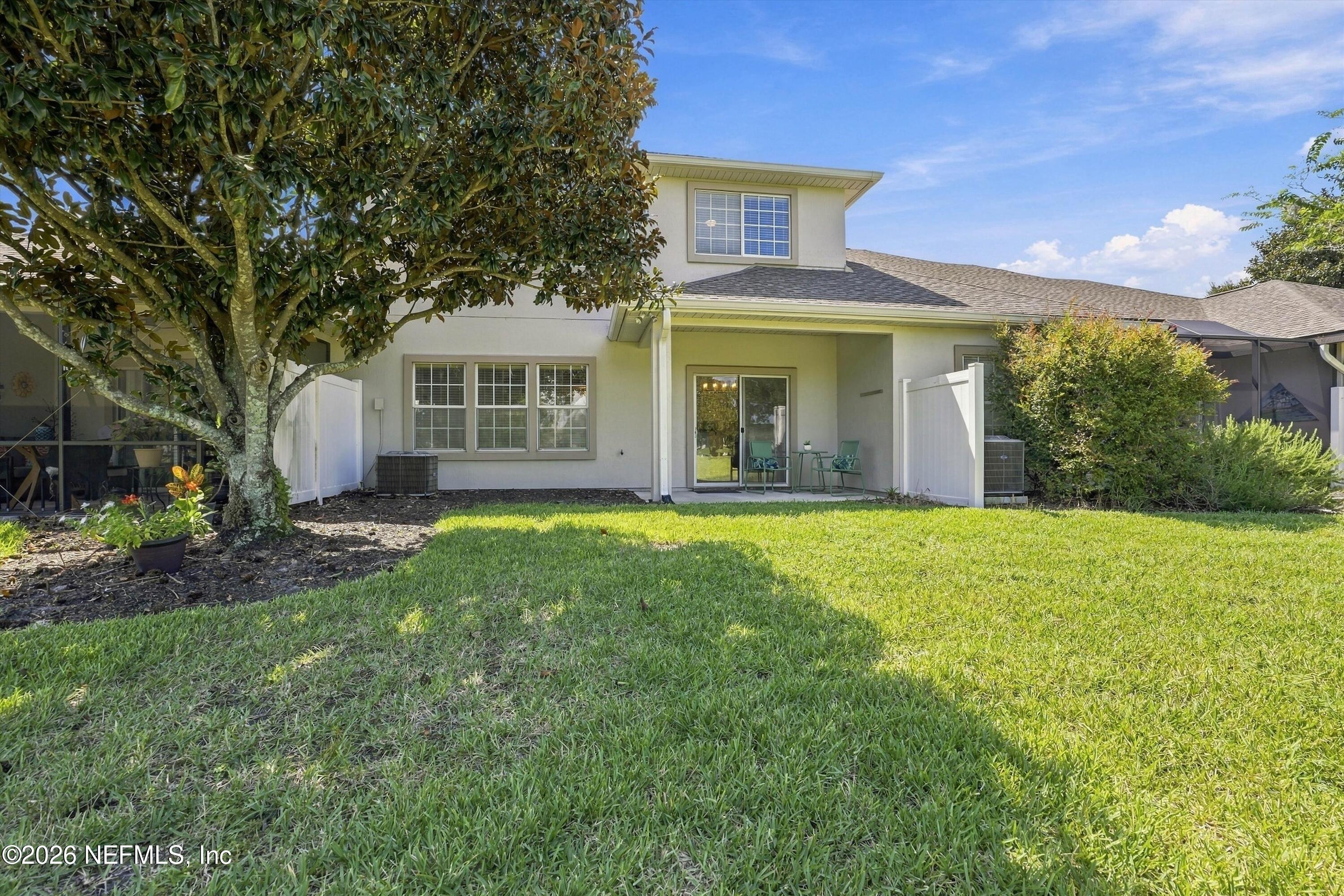 Rear of a two-story home with a covered patio, white fencing, and a large shaded lawn.