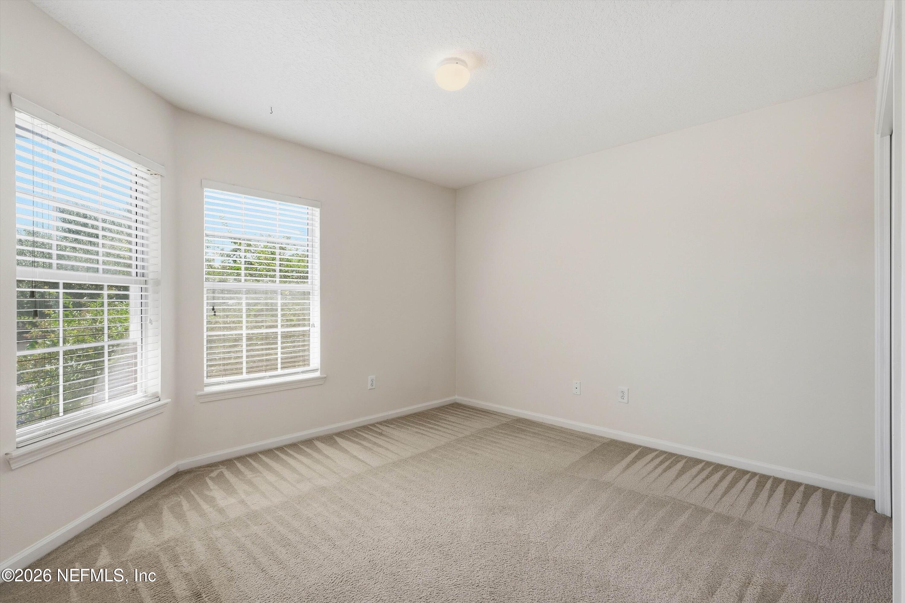 Empty bedroom with beige carpet and two windows with white blinds.