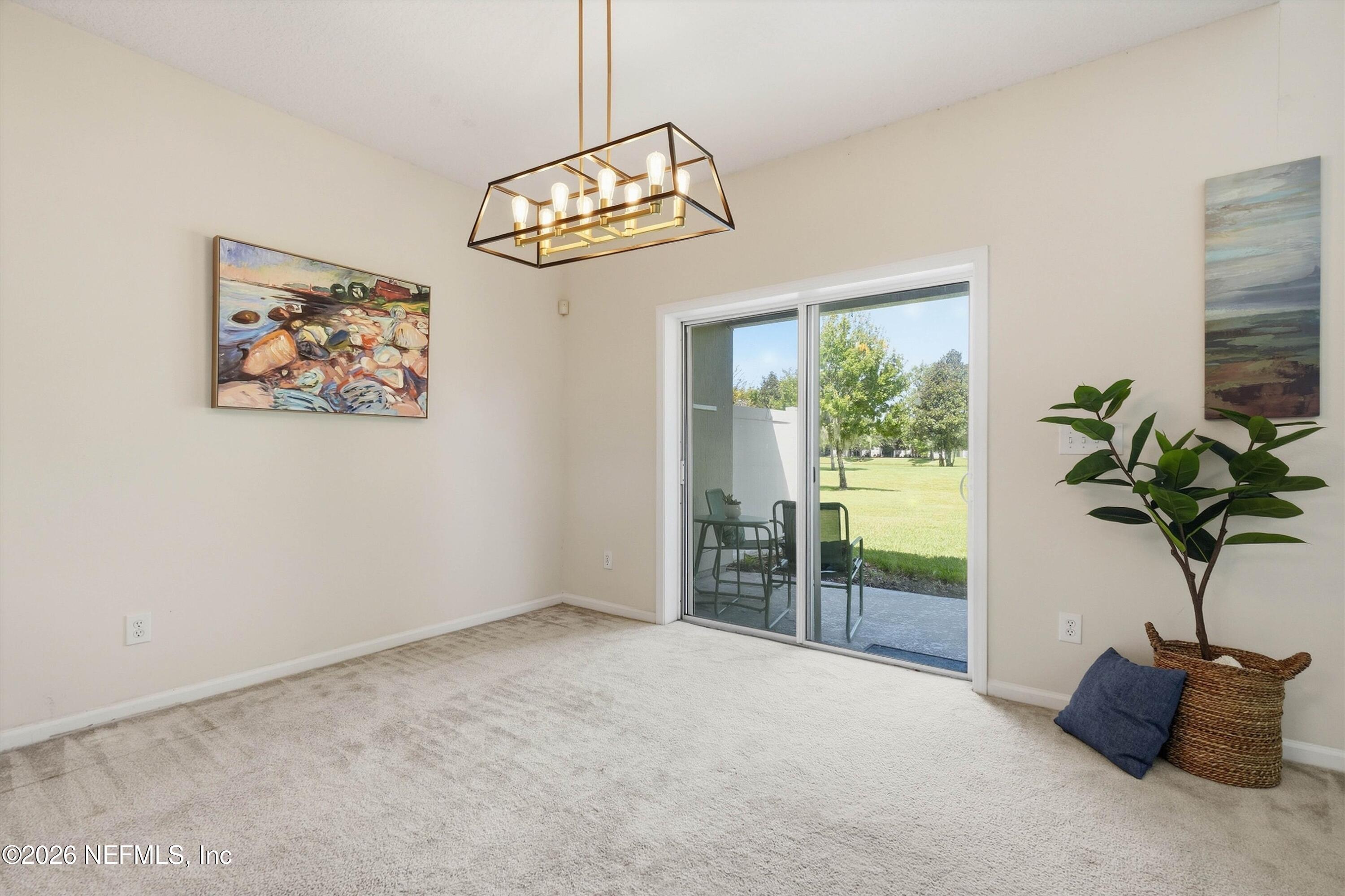 Carpeted dining area with a geometric chandelier and sliding glass doors to a patio and lawn.