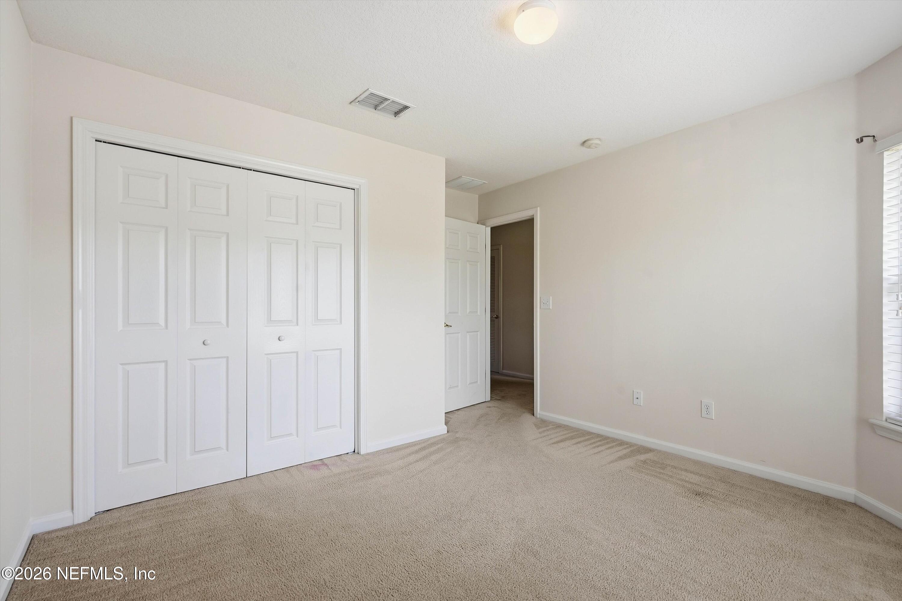 Empty bedroom with beige carpet, white closet doors, and a window with blinds.