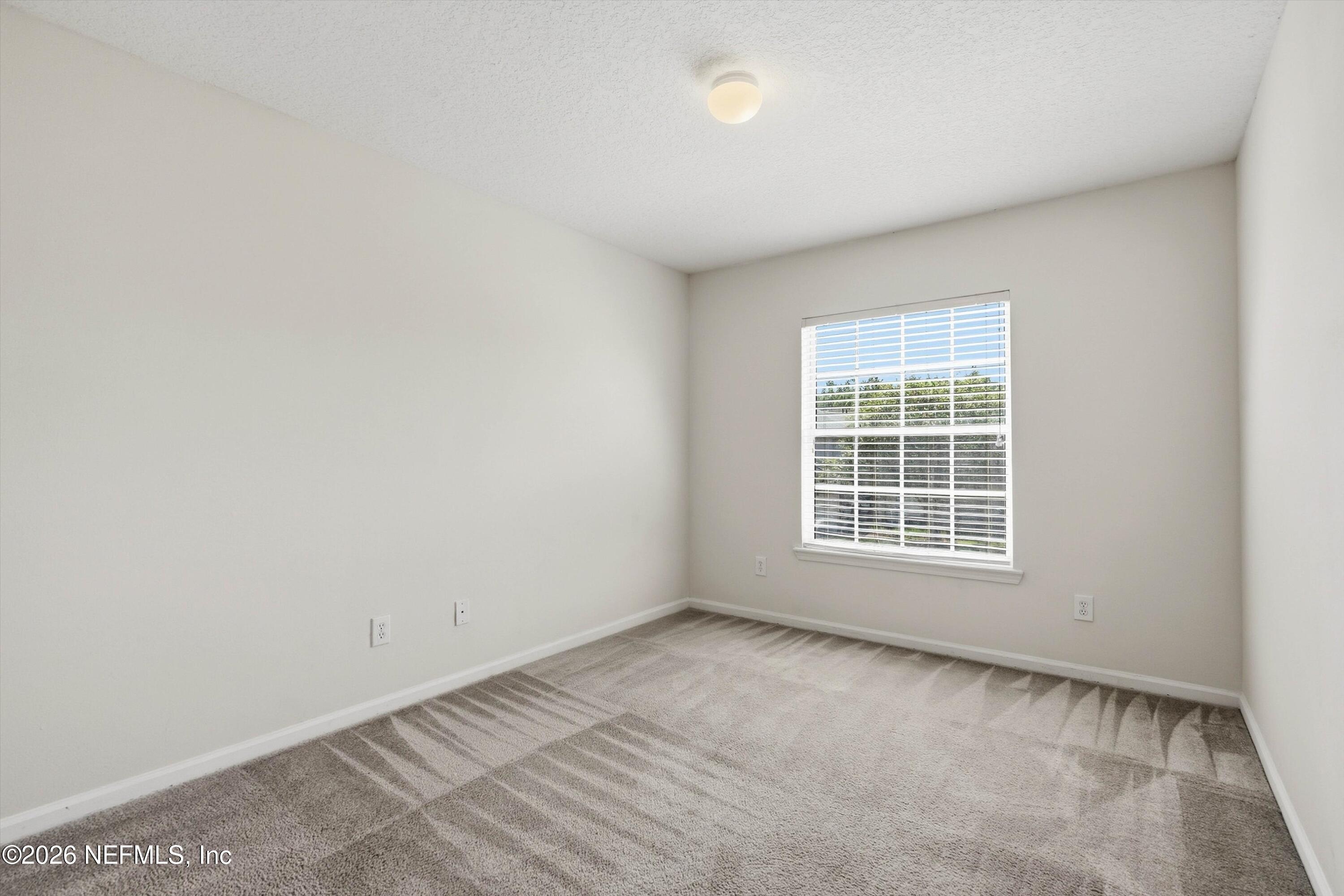 Empty bedroom with gray carpet and a window fitted with white blinds.