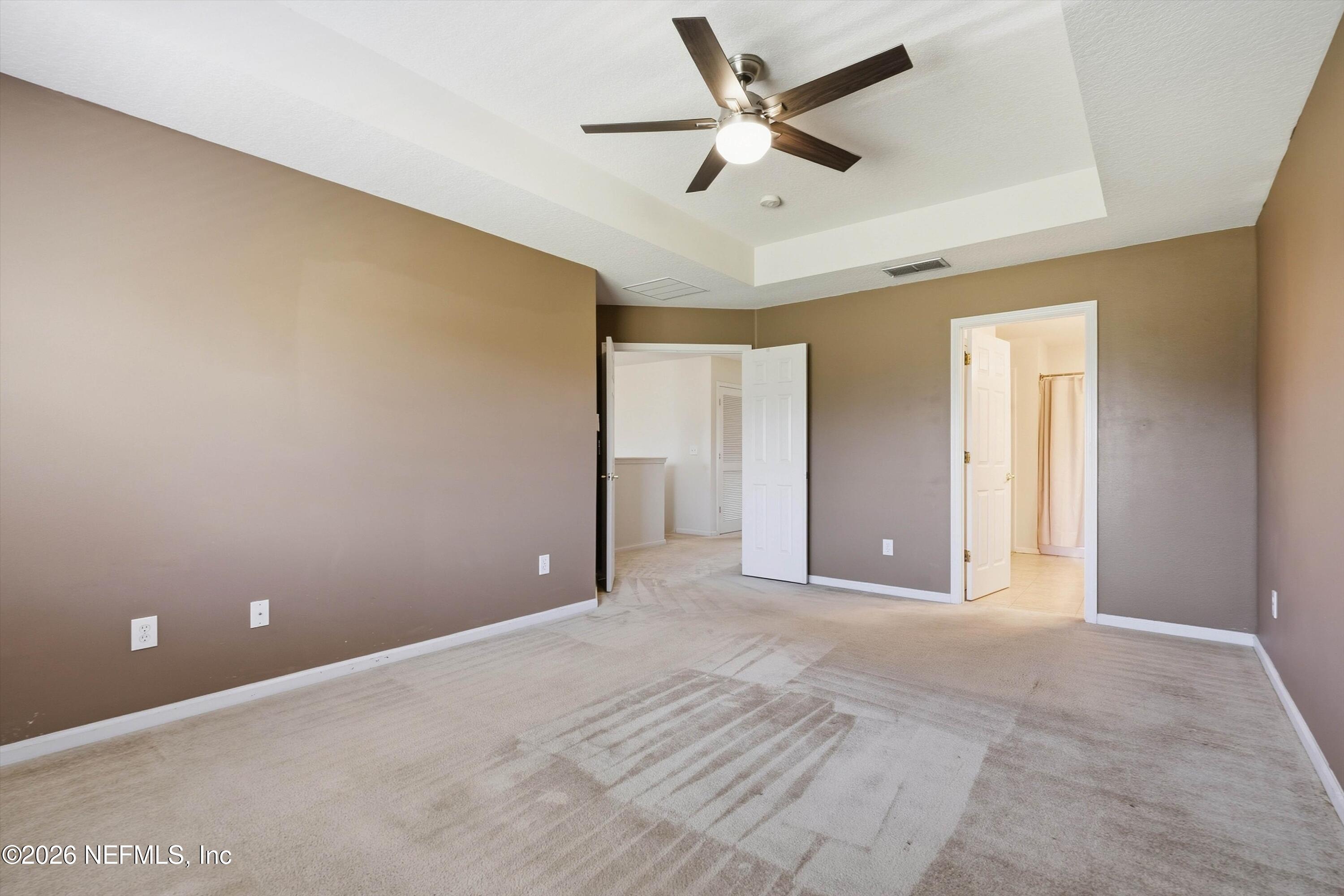 Empty bedroom with taupe walls, light carpet, a ceiling fan, and open doors.