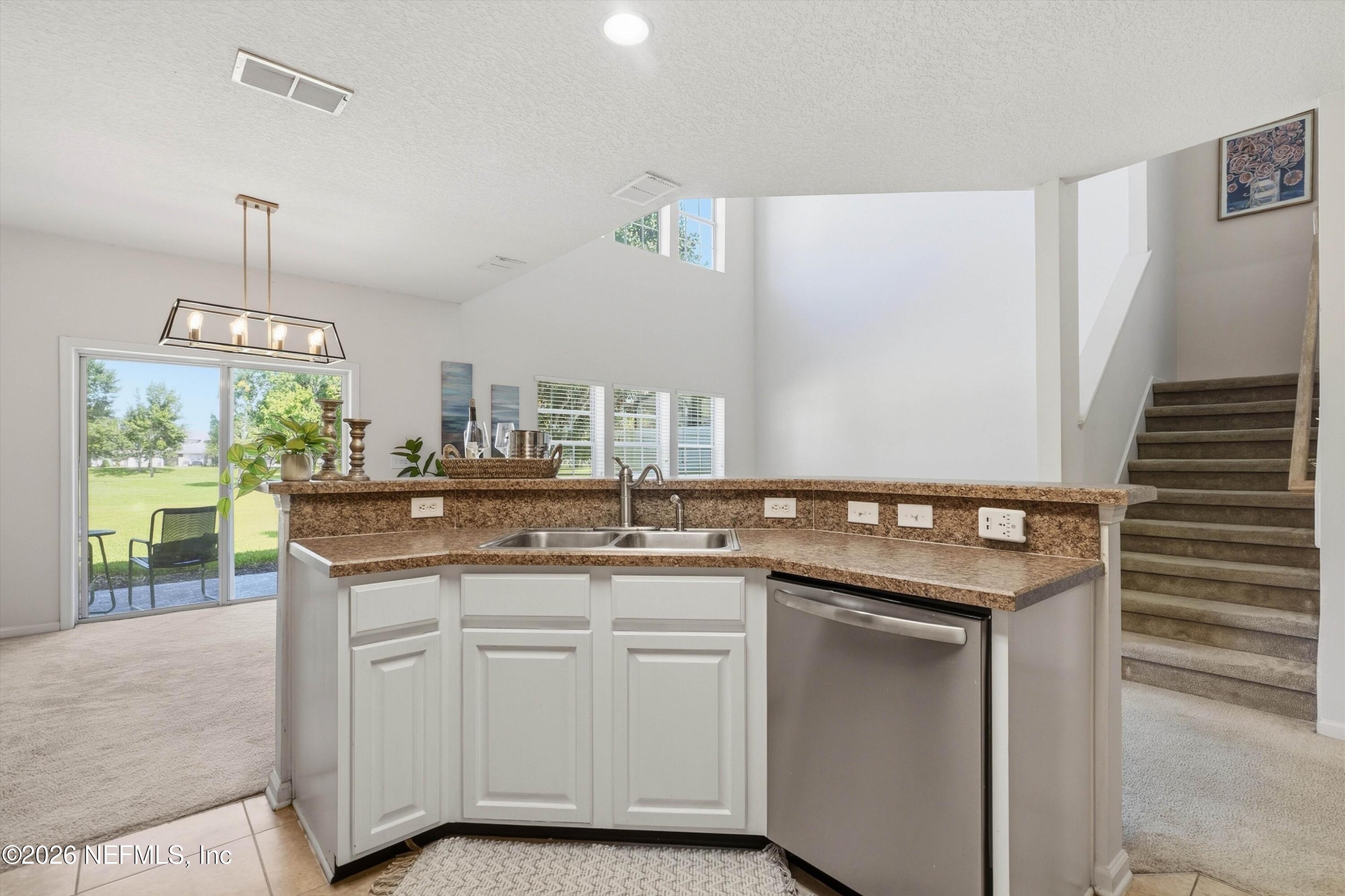 Open kitchen with brown stone counters, white cabinets, and a view to the lawn and staircase.