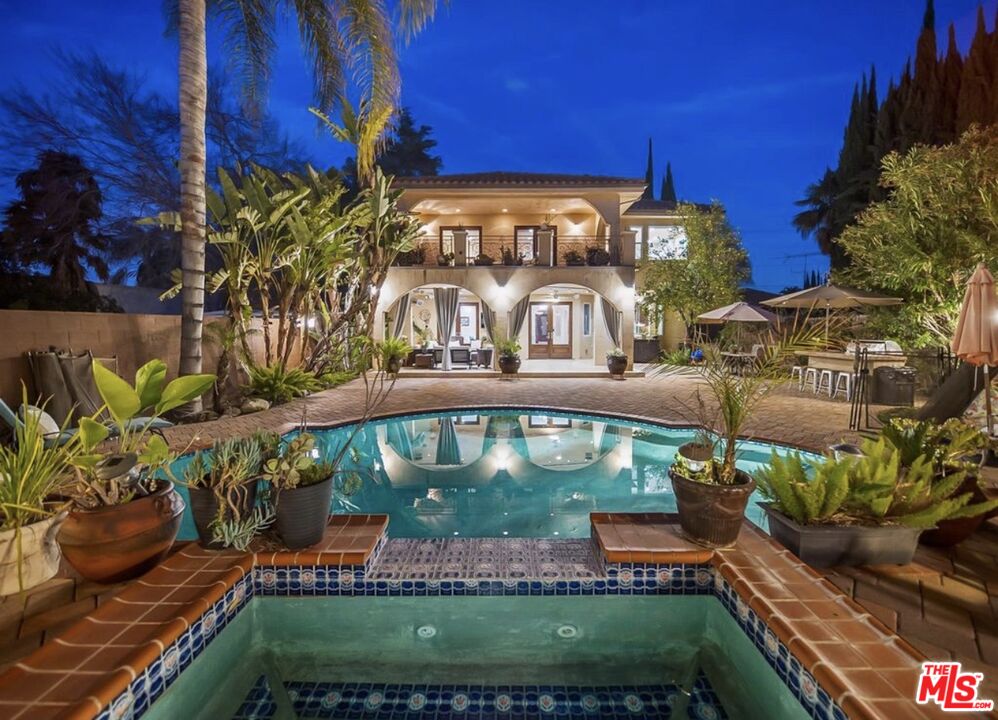 Two-story home with an illuminated balcony and arched patio doors behind a swimming pool.