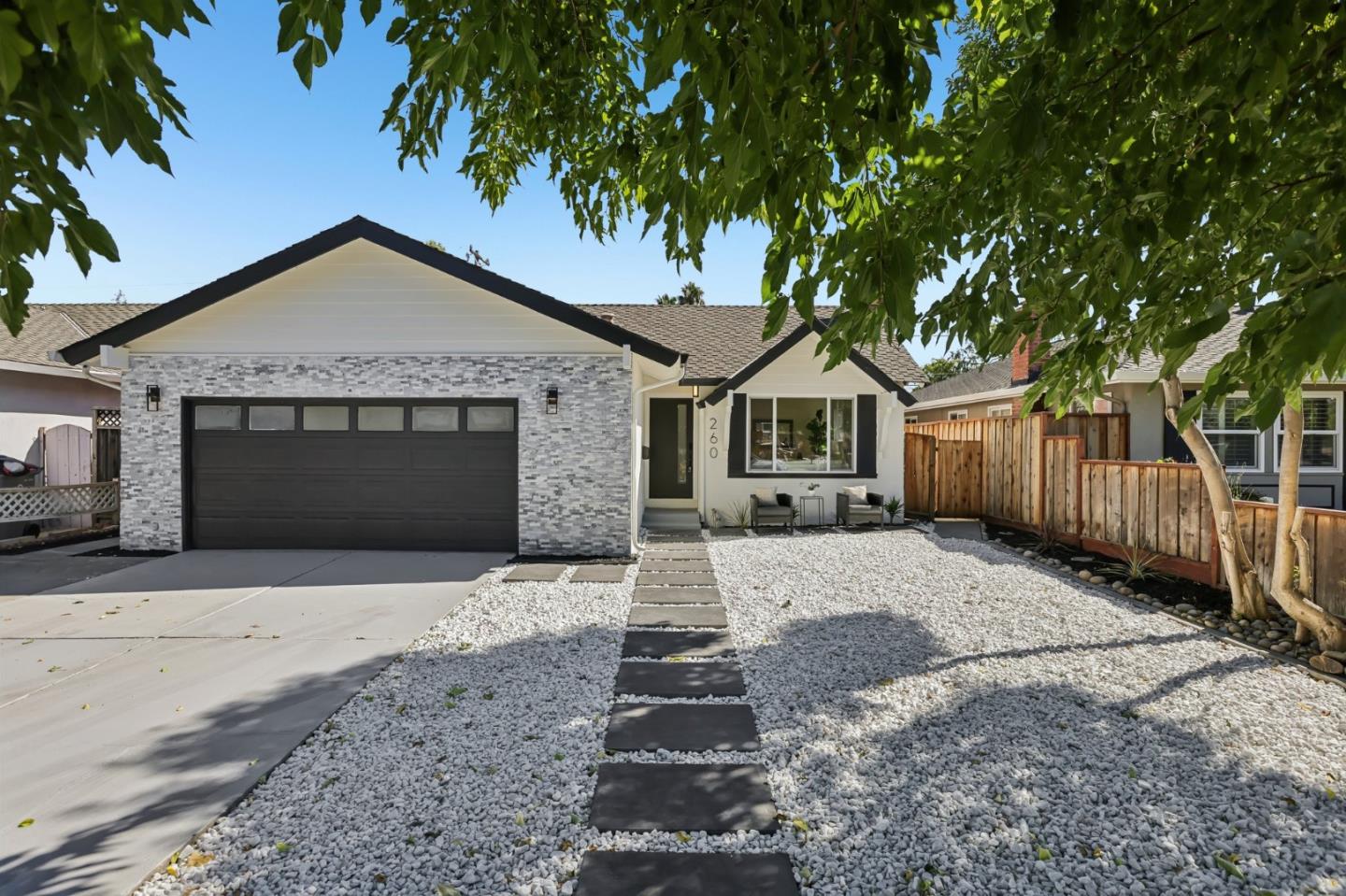 Single-story home with a stone facade, dark garage door, and gravel yard crossed by a stepping-stone path.
