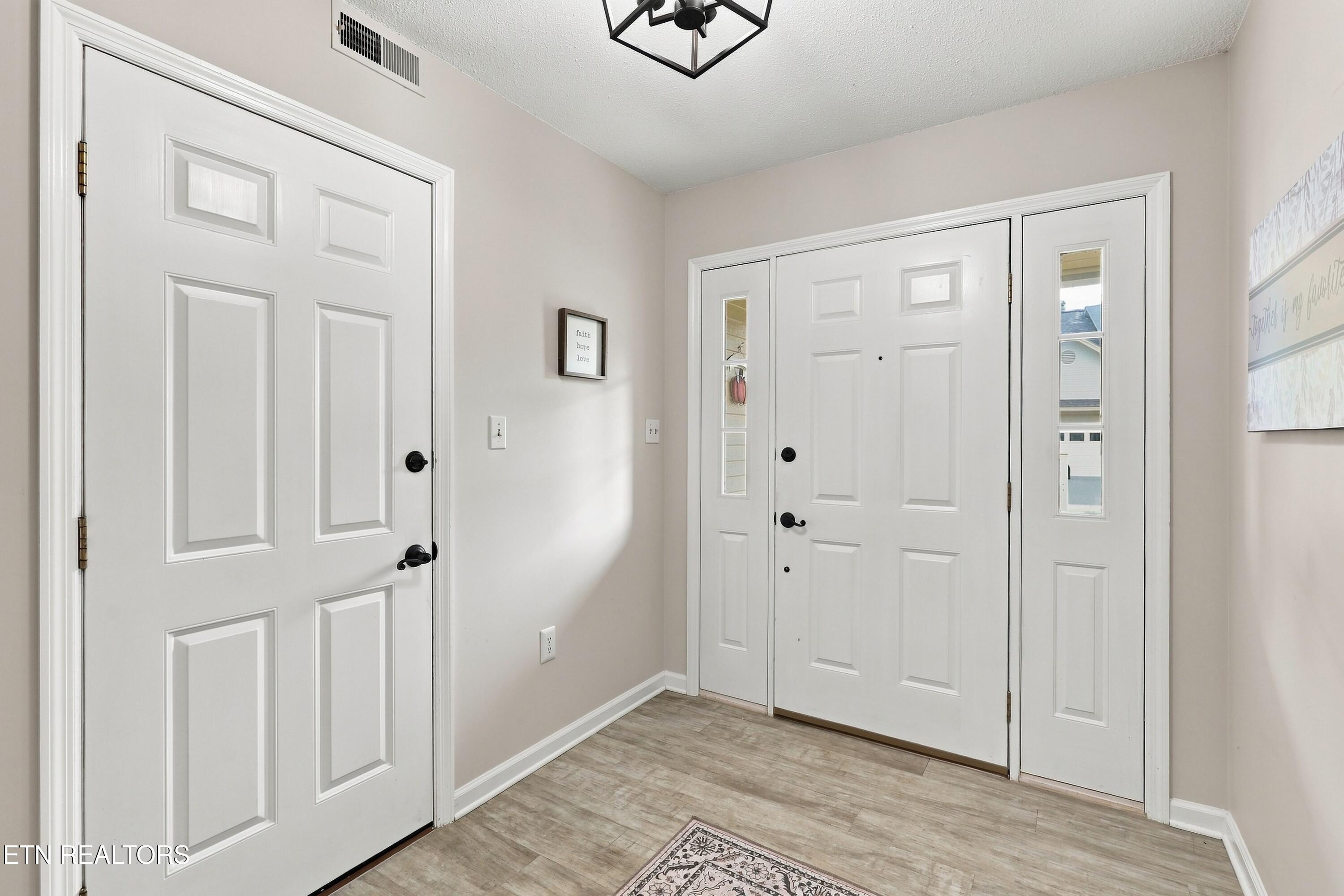 Entry foyer with white front door and glass sidelights, a second paneled door, and wood-look tile flooring.
