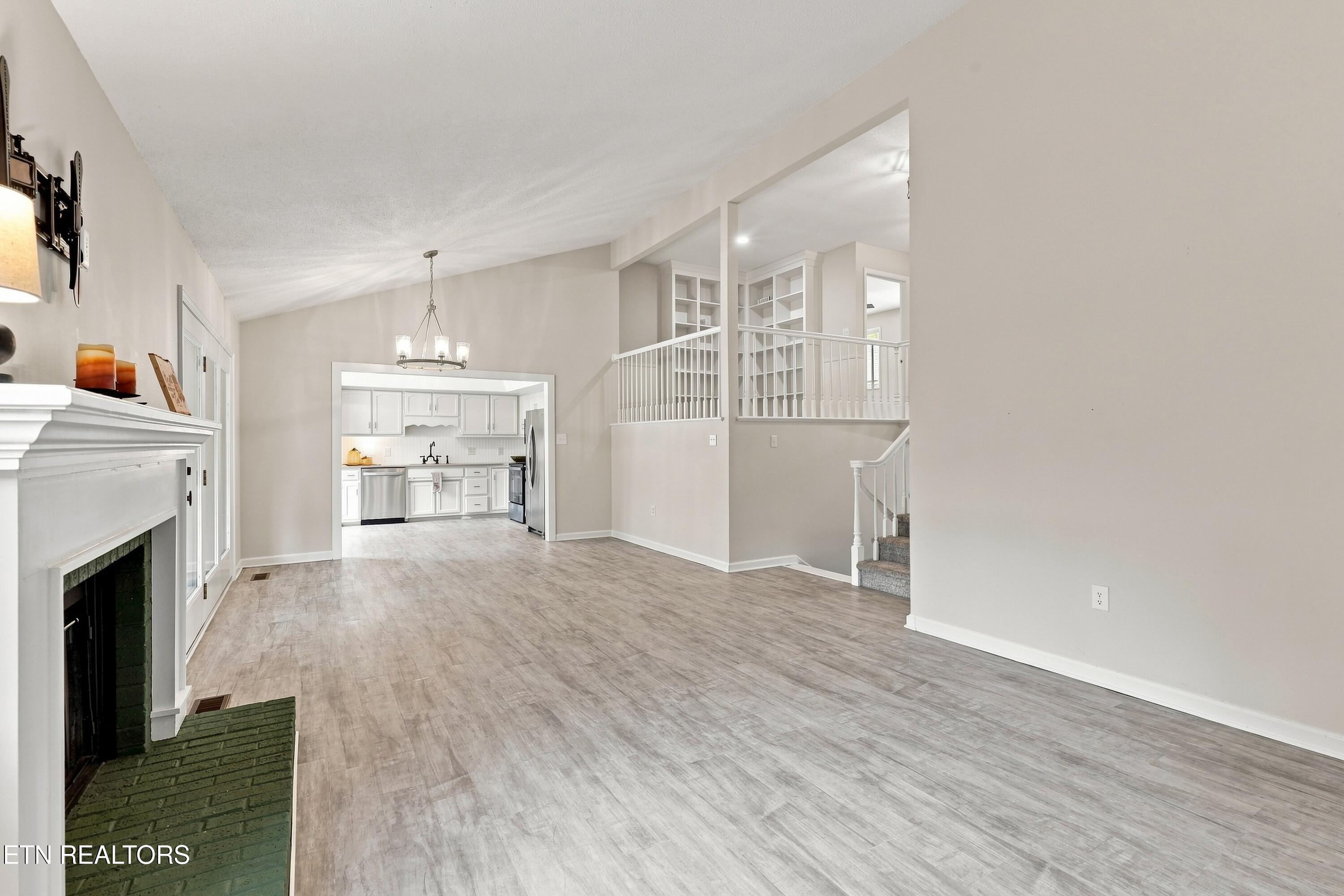 Open living room with a fireplace, vaulted ceiling, and view into the kitchen.