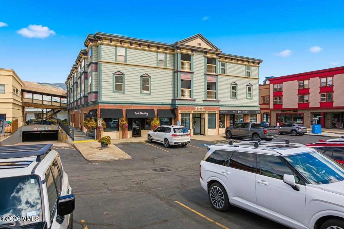 Multi-story pale green commercial building with ground-floor shops and a busy parking lot.