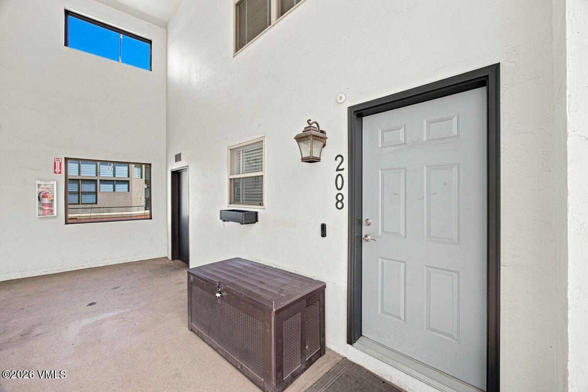 Covered unit 208 entry with a pale gray door, wall lantern, and storage bench.