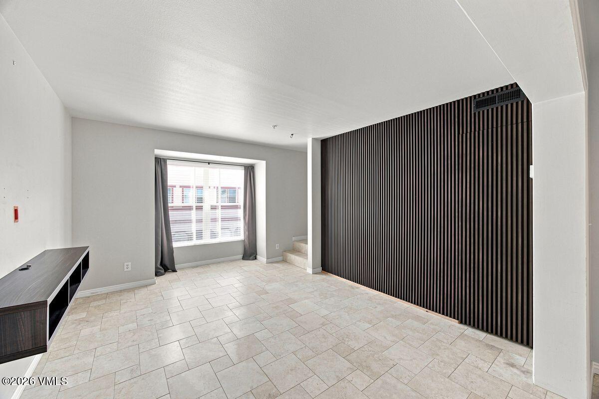 Vacant tiled room with a large curtained window, dark slat wall, and short staircase.