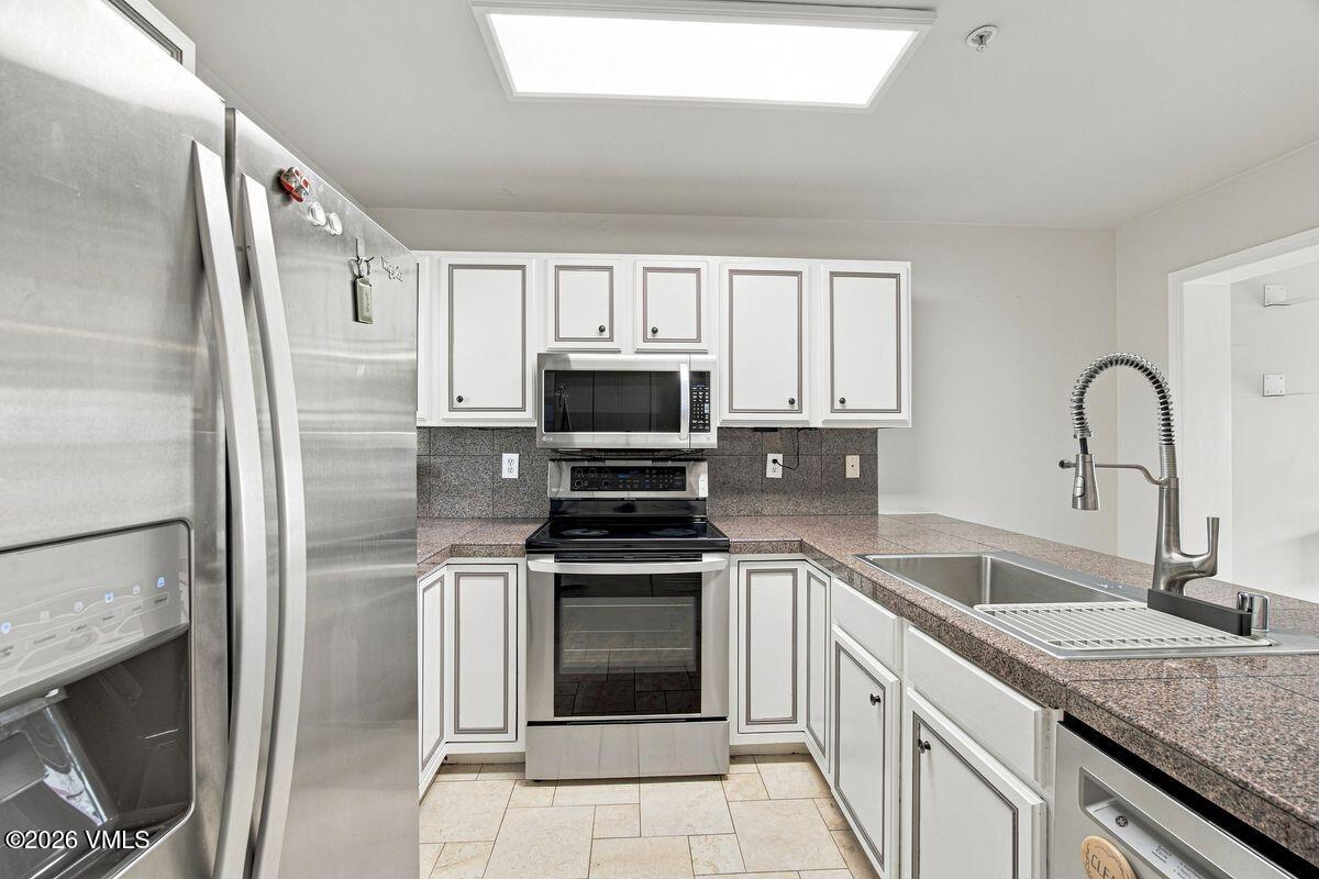 Kitchen with white cabinets, stainless steel appliances, stone counters, and a deep sink with a spring-coil faucet.