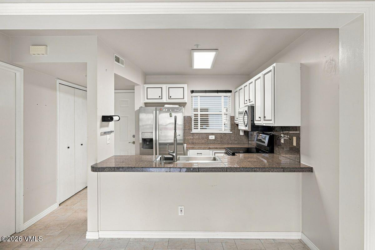 Kitchen with white cabinets, dark stone counters, breakfast bar, and stainless steel appliances.