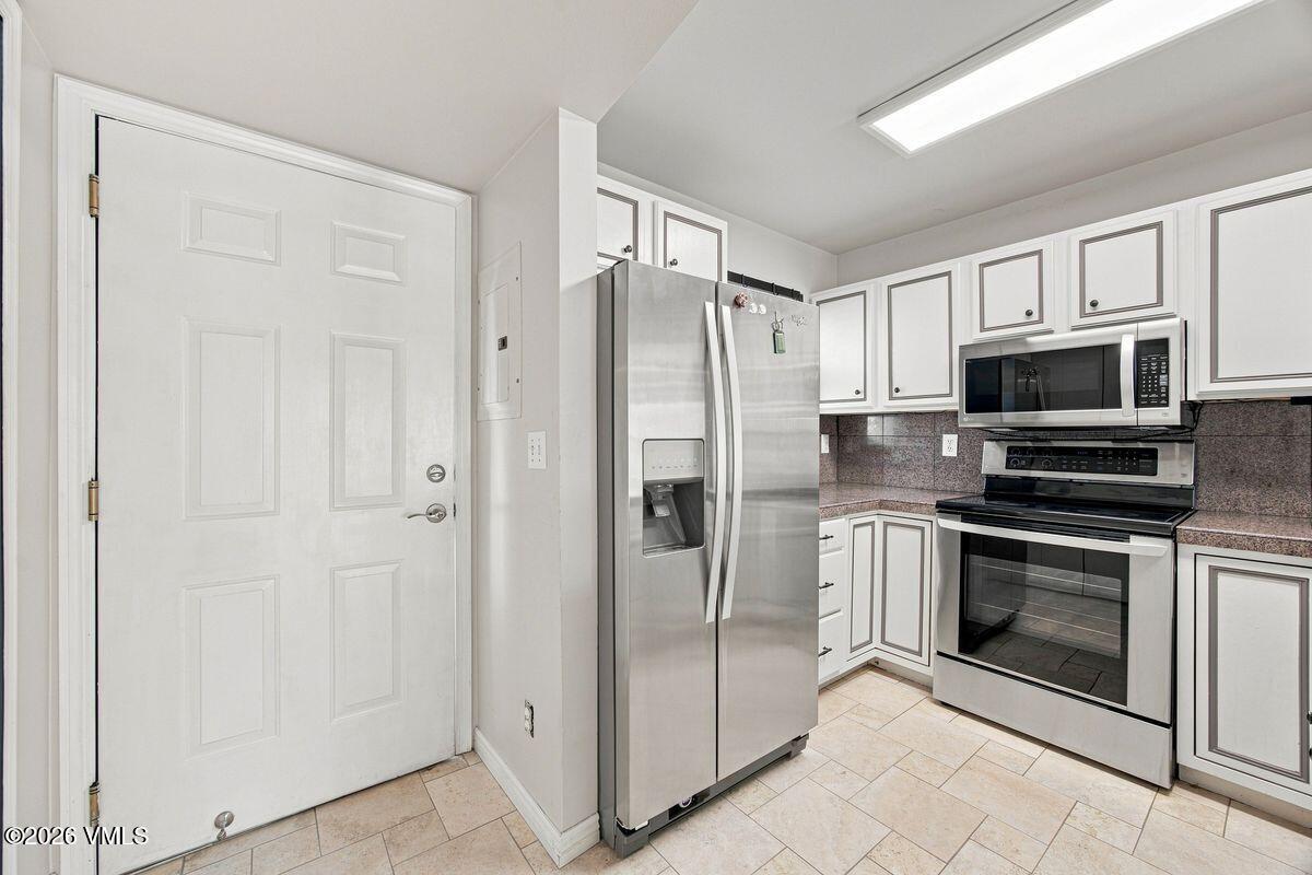Kitchen with white cabinets, dark countertops, and stainless steel appliances beside the entry door.