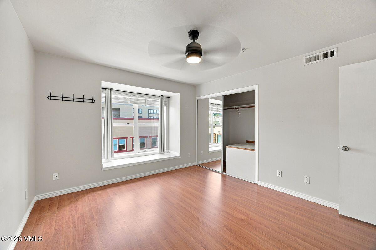 Vacant bedroom with wood flooring, a ceiling fan, large window, and open closet.