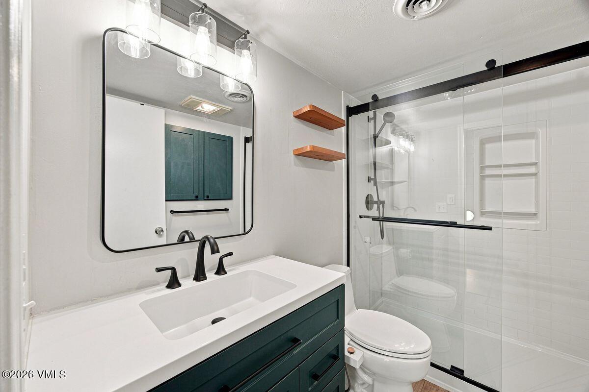 Bathroom with a dark teal vanity, black fixtures, and a glass-enclosed white-tile shower.