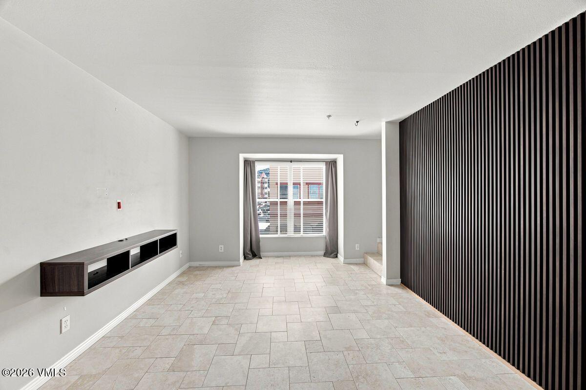 Vacant living area with tiled floors, a floating media console, slatted accent wall, and curtained window.