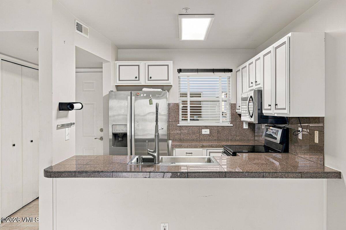 Kitchen with granite peninsula, stainless steel appliances, and white cabinetry.