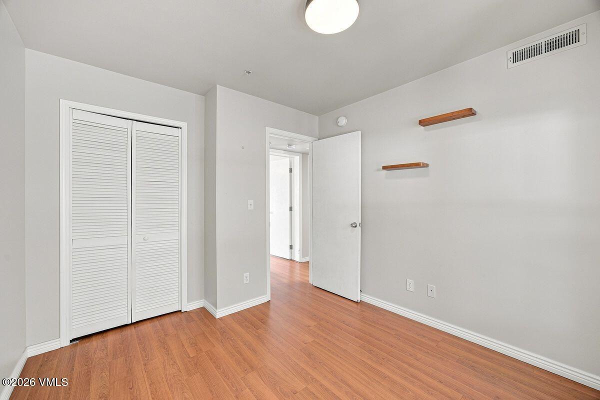 Empty room with warm wood flooring, a louvered closet, and two floating wooden shelves.
