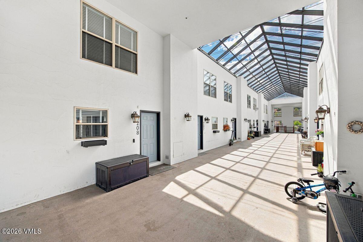 Residential corridor with unit 208 door beneath a high glass roof.