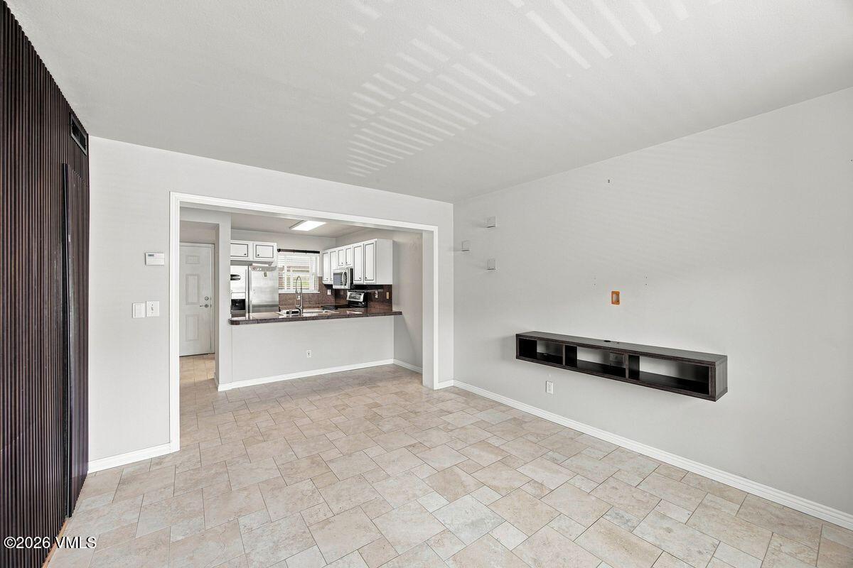 Unfurnished living area with beige tile flooring and a view into the kitchen.