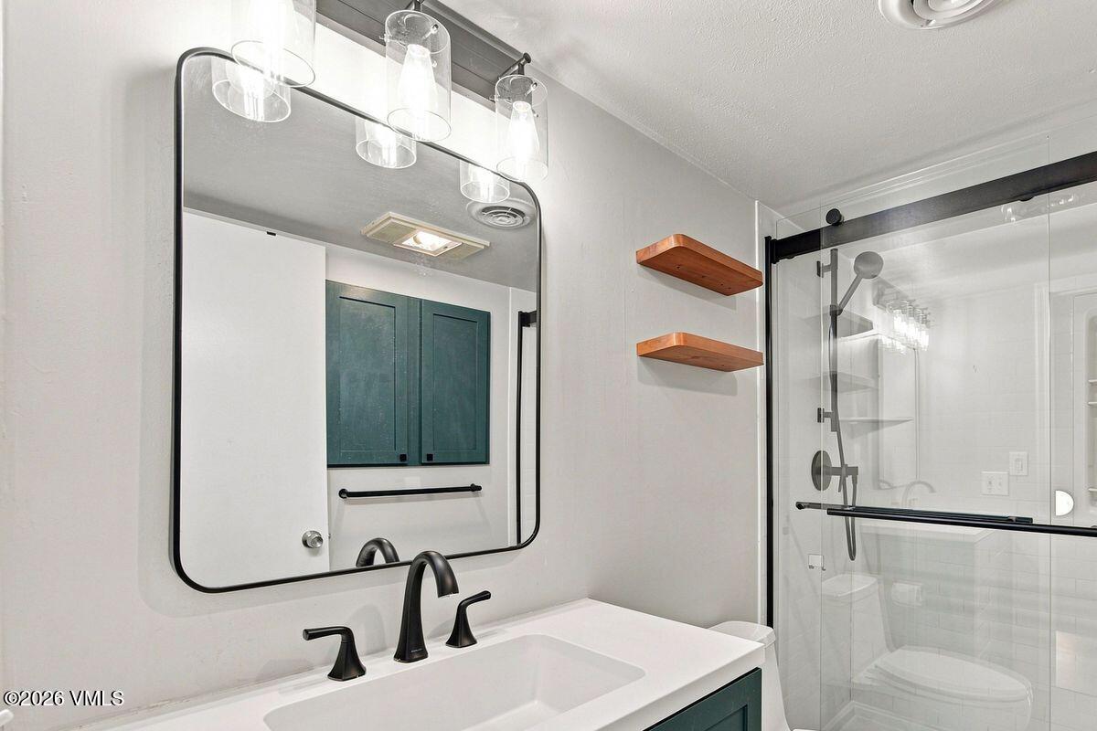 Bathroom with a white vanity, black fixtures, large mirror, and glass-enclosed shower.