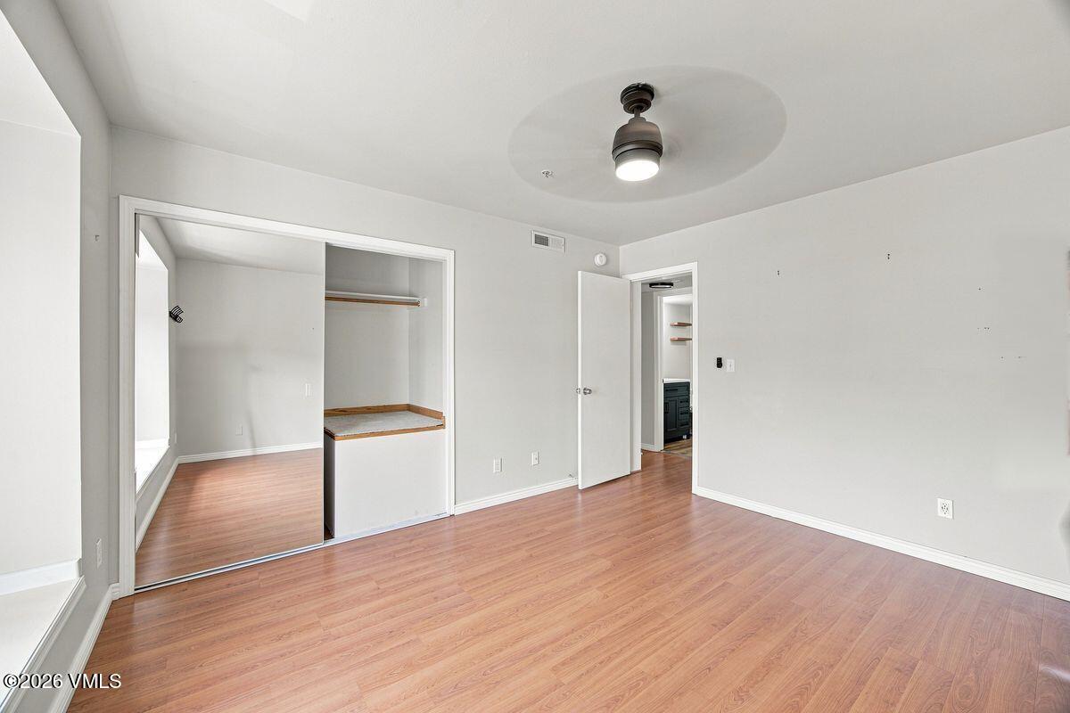 Vacant bedroom with wood-look flooring, a ceiling fan, and a wide sliding-door closet.