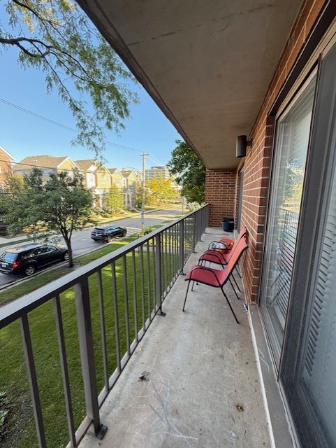 Apartment balcony with red chairs, black railing, and views of a tree-lined residential street.