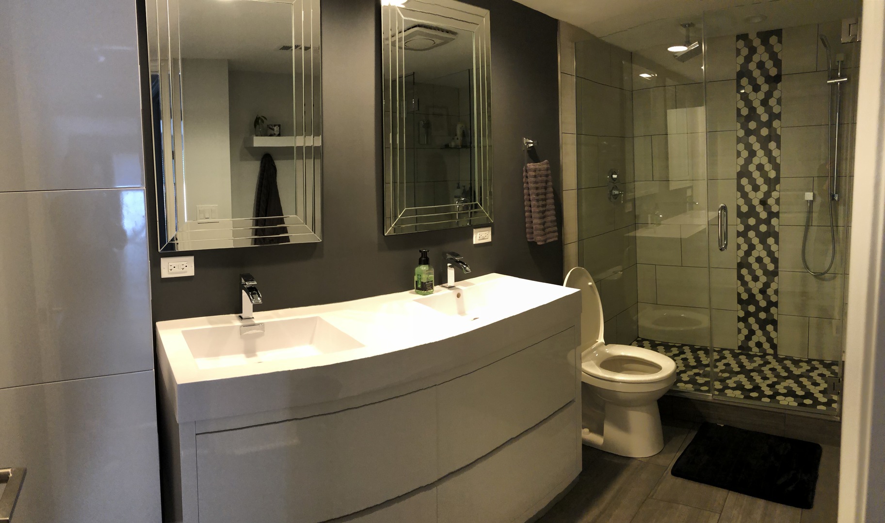 Bathroom with a double-sink vanity and glass shower featuring black-and-white hexagonal mosaic tile.
