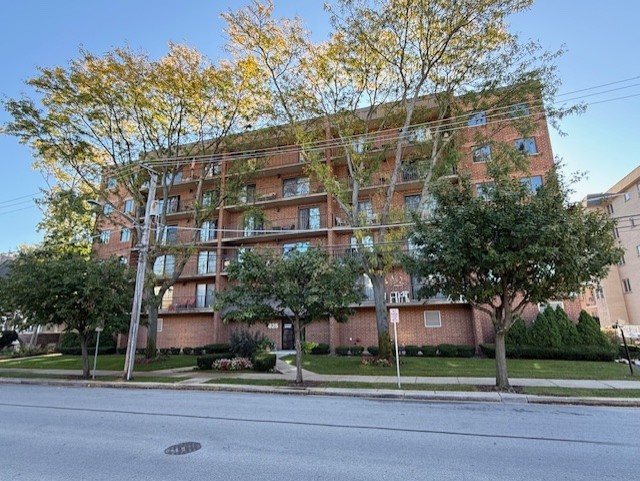 Red-brick apartment building with balconies, mature trees, and a lawn along the street.