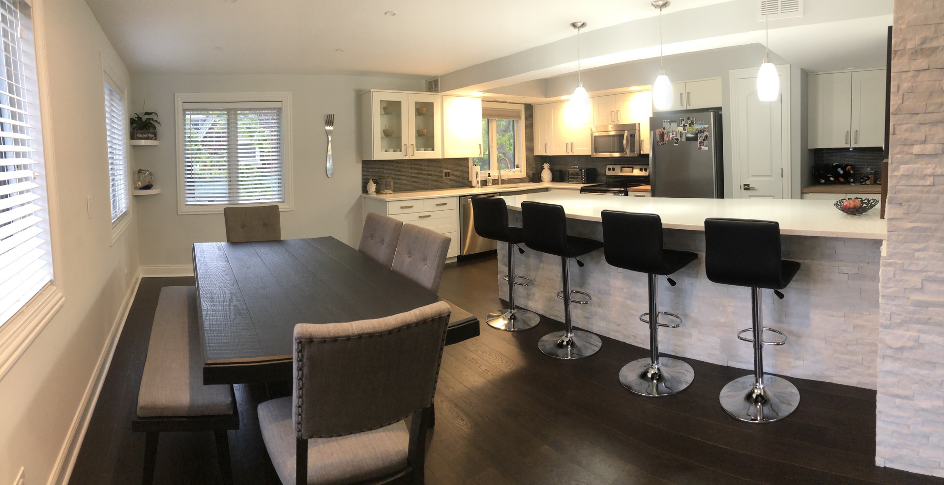 Open kitchen and dining area with a large breakfast island, black bar stools, and dark dining table.