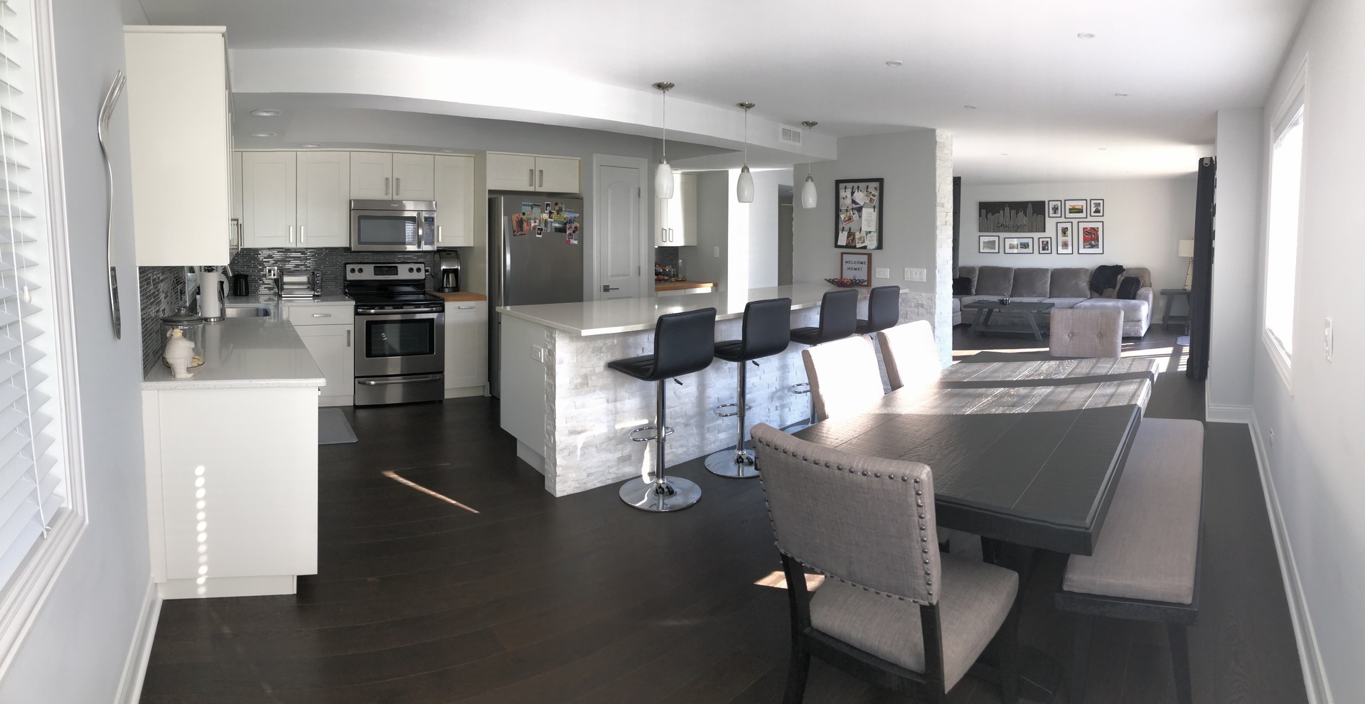 Open-plan condo kitchen, dining area, and living room with a stone-front breakfast bar and gray sectional.