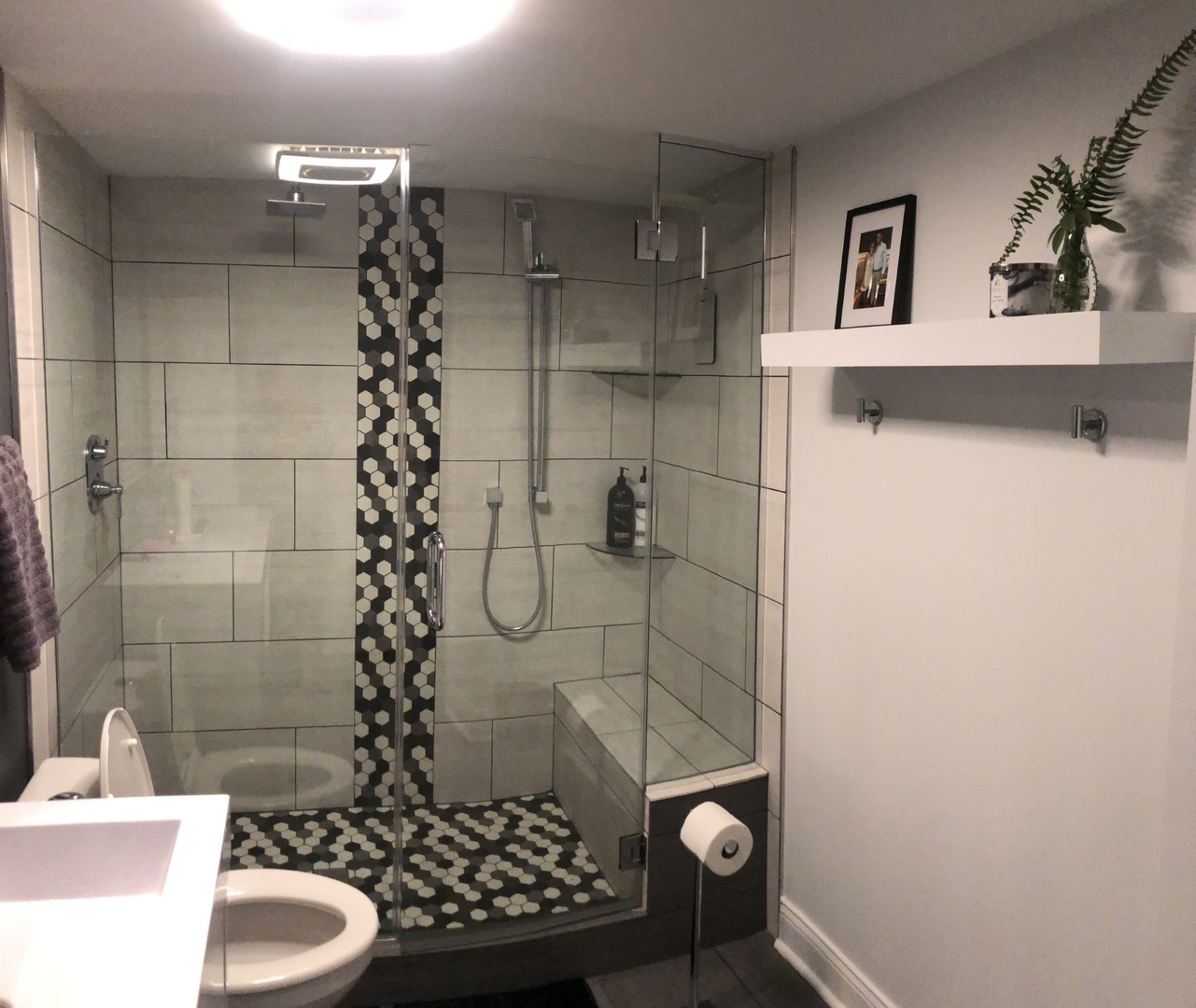 Bathroom with a glass walk-in shower, hexagonal tile accents, and floating shelf.