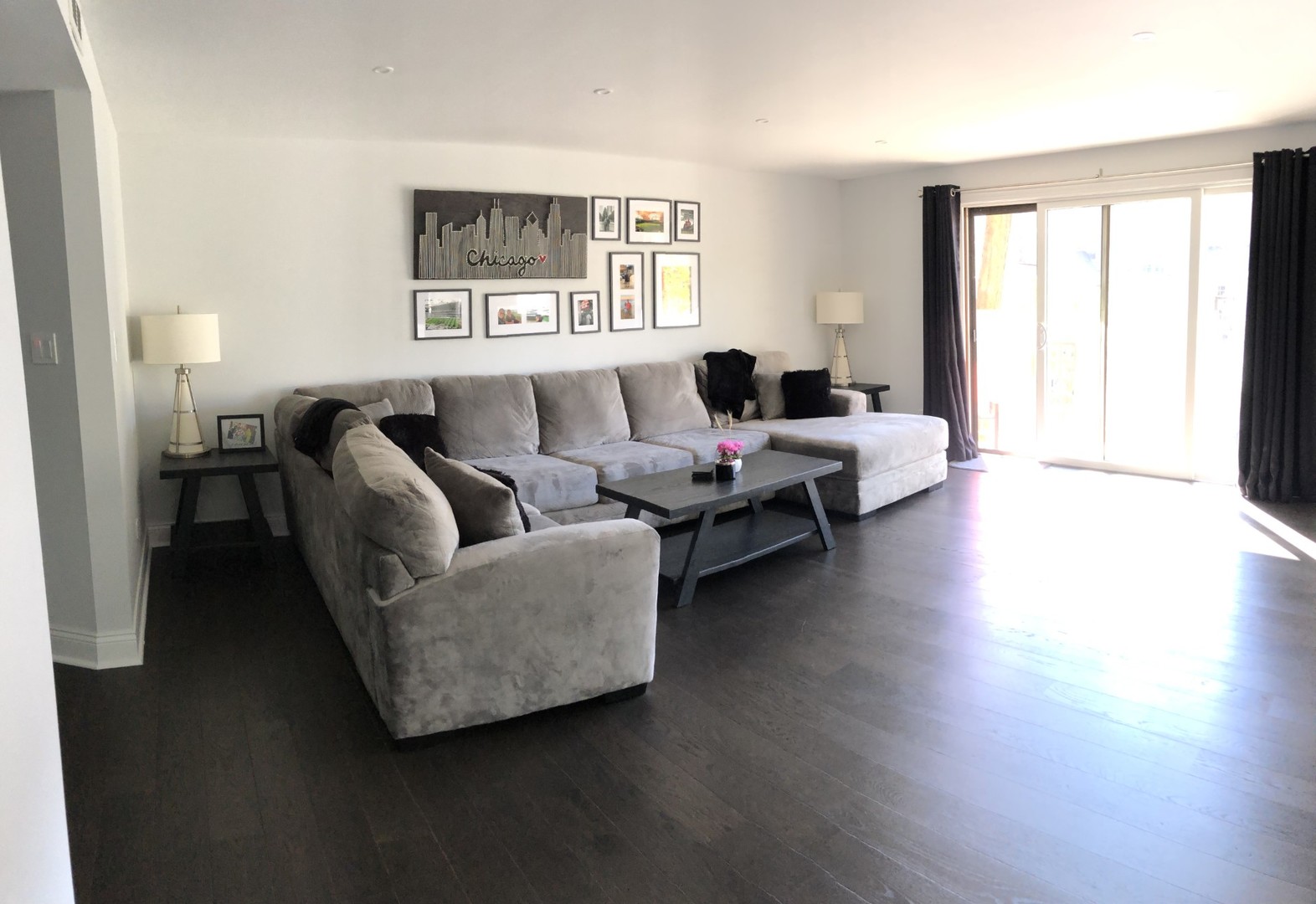 Living room with a large gray sectional, dark wood floors, and sliding glass doors.